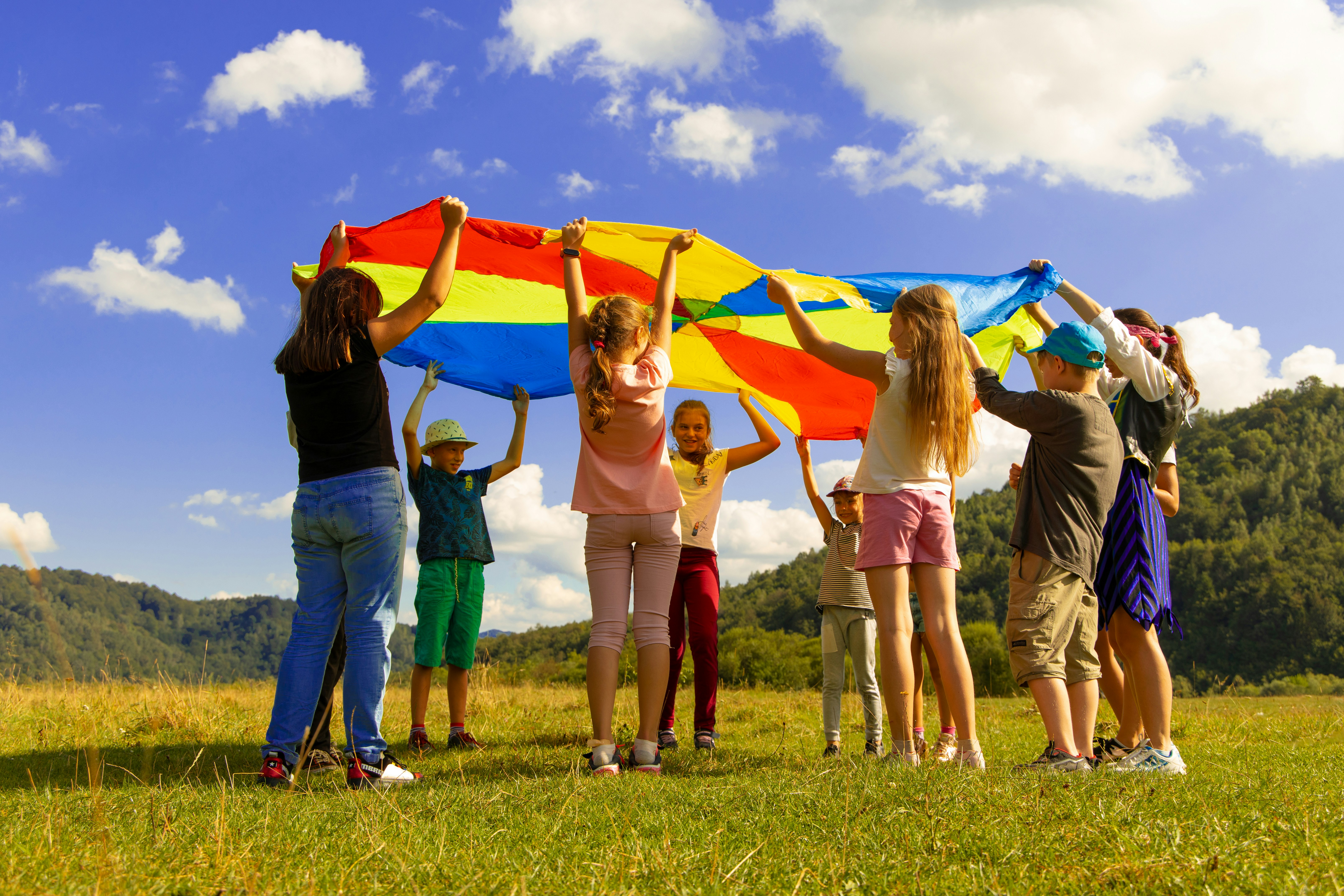 Image for the about page header - children holding a play parachute outsideo on a sunny day