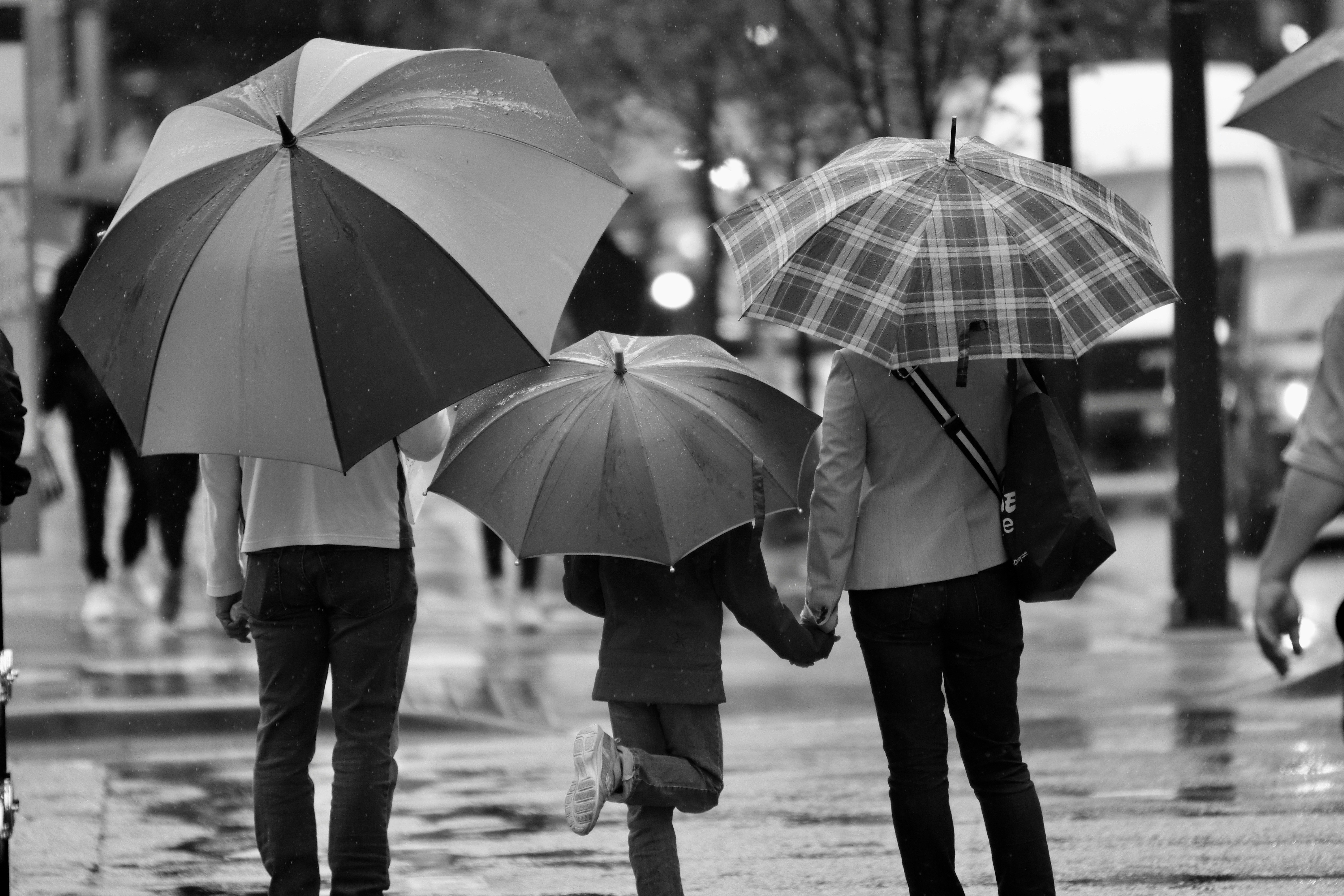 Header image for parents page - image of two parents walking with their child in the rain, all three are holding umbrellas